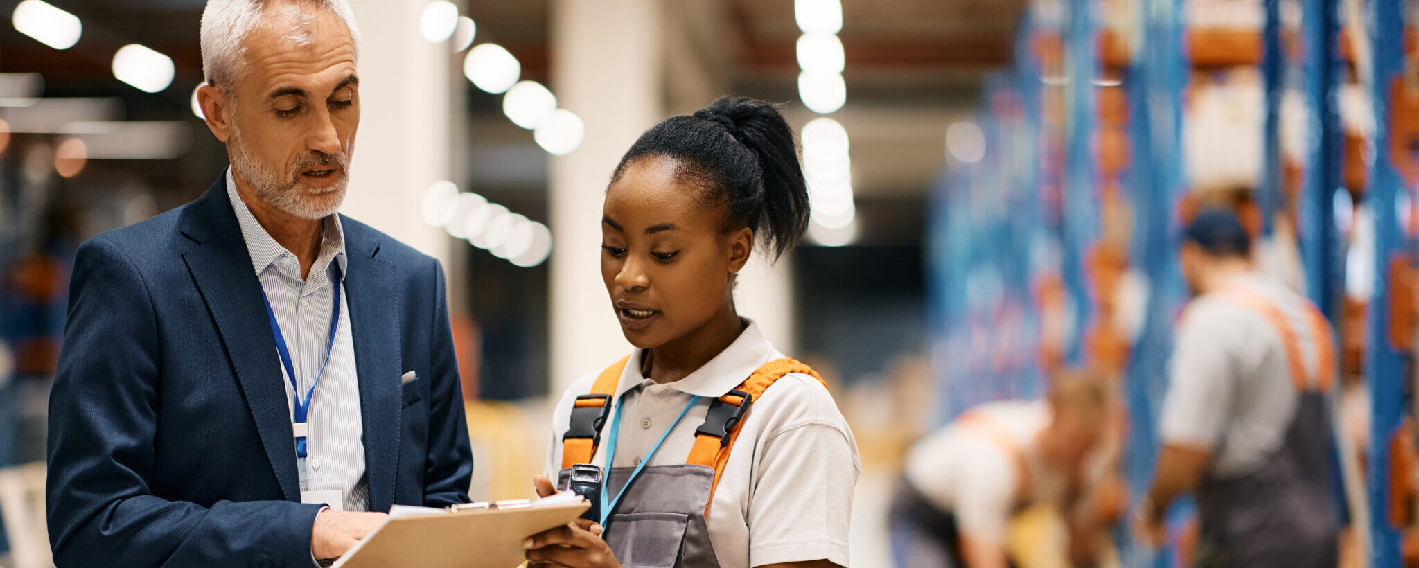 Mature Manager And Black Female Worker Going Through Paperwork In Distribution Warehouse.